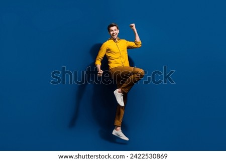 Full body photo of attractive young guy raise fists celebrate dressed stylish yellow clothes isolated on dark blue color background