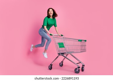 Full body photo of carefree overjoyed lady jumping push supermarket trolley isolated on pink color background