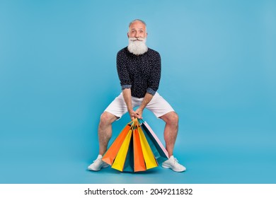 Full body photo of cheerful happy positive man hold heavy shopping bags isolated on blue color background