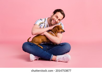 Full body photo of cheerful young happy man hold hands dog hug smile good mood isolated on pink color background