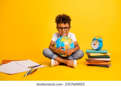 Full body photo of clever positive small kid sit floor hold world globe pile stack book clock notebook isolated on yellow color background - Powered by Shutterstock