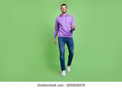 Full body photo of cool young brunet guy go wear hoodie jeans sneakers isolated on green background