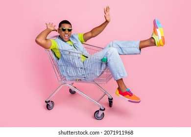 Full body photo of cool young brunet guy go in trolley wear eyewear t-shirt vest jeans shoes isolated pink background