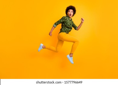 Full body photo of crazy dark skin curly lady jumping up high rushing fast home see street dangerous maniac wear green dotted shirt pants sneakers isolated yellow color background
