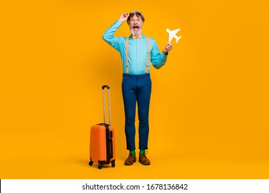 Full Body Photo Of Crazy Grandpa Hold Paper Plane Travel Rolling Suitcase Open Mouth Wear Sun Specs Blue Shirt Suspenders Bow Tie Pants Boots Socks Isolated Yellow Color Background