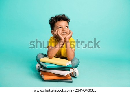 Full body photo of cute little boy look empty space lean on books pile wear trendy yellow clothes isolated on aquamarine color background