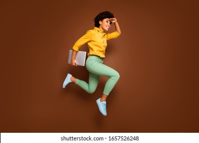 Full body photo of funky dark skin lady jump high hold notebook hurry lessons school see building close wear yellow shirt green pants footwear isolated brown color background