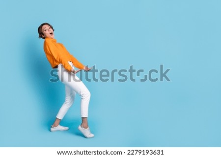 Full body photo of funky young woman carry heavy invisible box empty space dressed stylish orange look isolated on blue color background