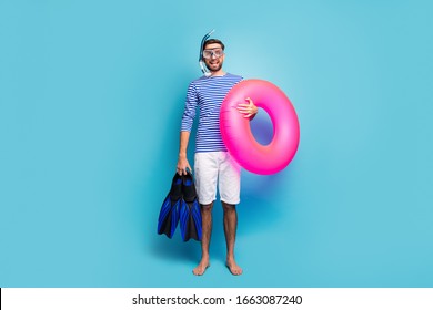 Full body photo of funny excited guy tourist swimmer hold underwater mask breathing tube flippers pink lifebuoy wear striped sailor shirt shorts isolated blue color background