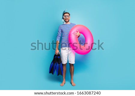 Full body photo of funny excited guy tourist swimmer hold underwater mask breathing tube flippers pink lifebuoy wear striped sailor shirt shorts isolated blue color background