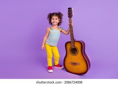 Full body photo of funny little brunette girl with guitar wear top pants shoes isolated on violet color background