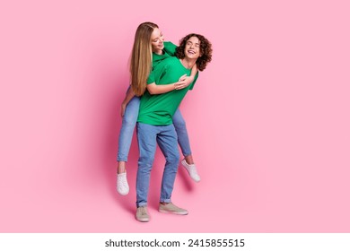 Full body photo of funny smiling brunet curly hair teen guy holding hands happy girl ride piggyback isolated over pink color background - Powered by Shutterstock