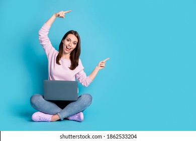 Full body photo girl sit floor legs crossed work laptop point index finger copyspace direct way follow comment ads wear lilac violet pullover denim jeans isolated blue color background