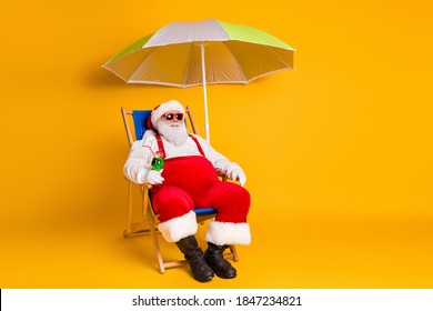 Full Body Photo Of Grey White Hair Bearded Santa Claus Chill Chaise-lounge Hold Cocktail X-mas Christmas Eve Noel Time Rest Wear Hat Pants Boots Isolated Bright Shine Color Background