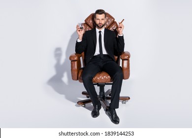 Full body photo of handsome business guy sit big office chair hold whiskey glass cuban cigar luxury chief wear black blazer pants tie shirt shoes suit isolated grey background - Powered by Shutterstock