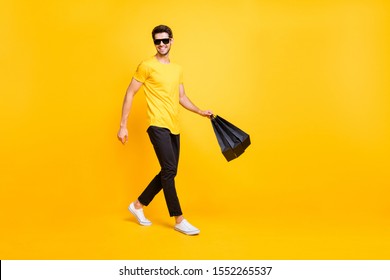 Full Body Photo Of Handsome Guy Carry Boutique Bags Make Abroad Shopping Go Fashionable Mall Wear Casual T-shirt Black Pants Isolated Yellow Color Background
