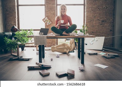 Full Body Photo Of Happy Trader Woman Sit On Table Crossed Legs Feel Carefree Careless Rest Relax Hold White Coffee Cup In Messy Office Loft