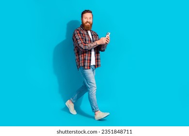 Full body photo of intelligent man with beard dressed checkered shirt go to empty space hold smartphone isolated on blue color background - Shutterstock ID 2351848711