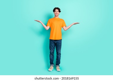 Full body photo of nice brown hair millennial guy stand hold empty space wear t-shirt jeans sneakers isolated on blue background