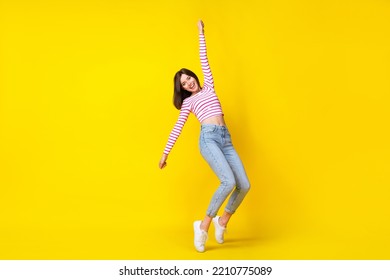 Full body photo of nice young girl raise arm hang hold invisible parasol dressed trendy striped outfit isolated on yellow color background