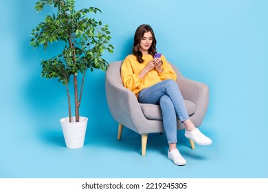Full body photo of nice young lady sit armchair hold device chatting relaxing dressed stylish yellow look isolated on blue color background