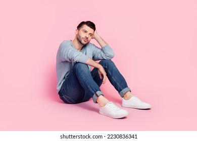 Full body photo of nice young guy sitting depressed dreaming bored thoughtful dressed trendy blue clothes isolated on pink color background