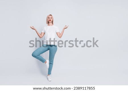 Full body photo of peaceful focused woman wear stylish t-shirt eyes closed stand in meditation pose isolated on gray color background