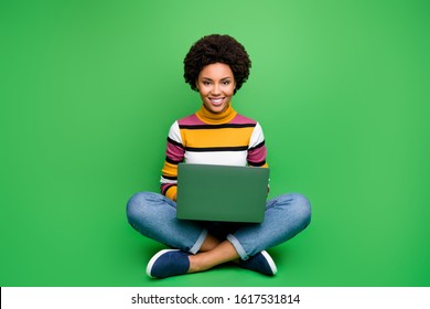 Full body photo of positive afro american girl sit legs crossed folded work on computer smm worker concept wear stylish denim jeans outfit isolated over green color background