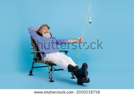 Full body photo of positive relaxed old man sit chair vacation fisherman isolated on blue color background