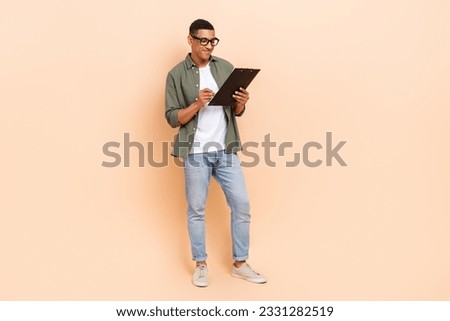 Full body photo of positive successful guy hold pen write clipboard empty space ad isolated on beige color background