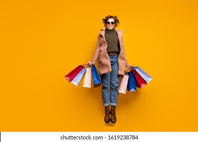 Full body photo of pretty funny lady jumping high up shopping center hold packs wear sun specs casual pink coat pullover jeans leopard print shoes isolated yellow color background - Shutterstock ID 1619238784