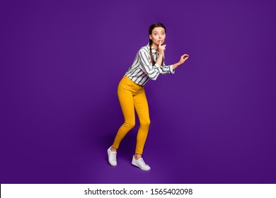 Full body photo of pretty lady holding finger on lips going tiptoes unexpected surprise visit wear striped shirt yellow trousers isolated purple color background - Shutterstock ID 1565402098
