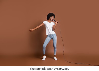 Full body photo of pretty positive dark skin lady hand hold mic singing loud isolated on brown color background - Powered by Shutterstock