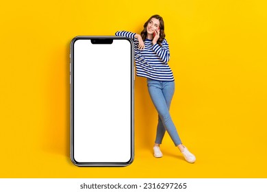 Full body photo of pretty young girl lean on big telephone talk phone dressed stylish striped look isolated on yellow color background - Powered by Shutterstock