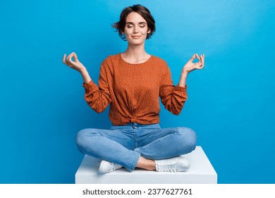 Full body photo of pretty young girl sit white platform meditation pose wear trendy brown outfit isolated on blue color background - Powered by Shutterstock