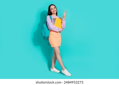 Full body photo of pretty young girl hold copybooks v-sign wear trendy violet outfit isolated on cyan color background - Powered by Shutterstock