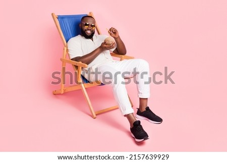 Full body photo of satisfied handsome guy enjoy cocktail sit chaise lounge isolated on pink color background