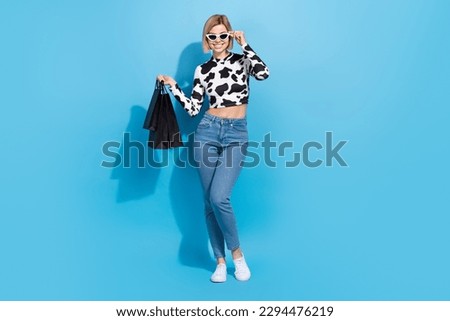 Full body photo of shopaholic girl wear denim jeans top dalmatian print touch sunglasses bags from zara isolated on blue color background