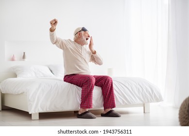 Full body photo of sleepy elderly man pensioner sit bed home indoors wake-up stretching yawn wear pajamas