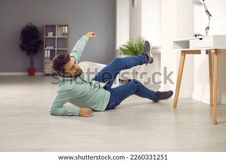 Full body photo of a young clumsy brunette man with unshaven bristles falling down to the floor and injuring his arm at home or in the office at his workplace and wearing casual clothes... Foto d'archivio © 