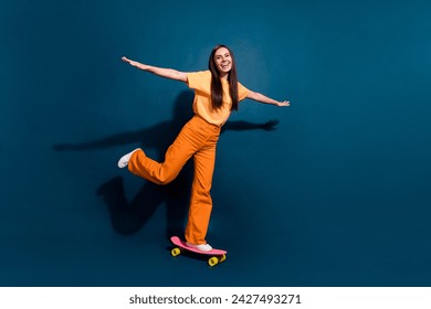 Full body photo of young girl wearing orange t shirt and pants keep balance standing penny board isolated on dark blue color background - Powered by Shutterstock