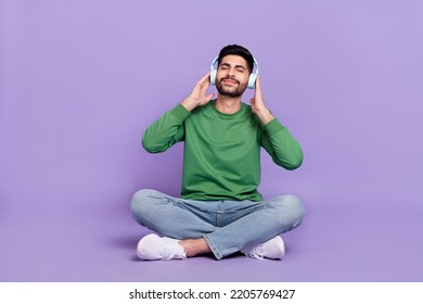 Full body photo of young hispanic man sit legs crossed enjoy music headphones wear trendy green garment isolated on violet color background - Powered by Shutterstock