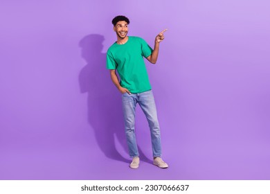 Full body photo of young man wear green t-shirt directing finger empty space enjoy new movie trailer isolated on violet color background