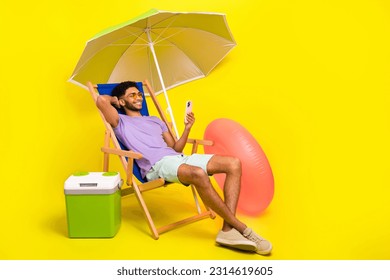 Full body photo of young man sit chair browsing his smartphone rest near fridge with beer wear t-shirt shorts isolated on yellow background - Powered by Shutterstock