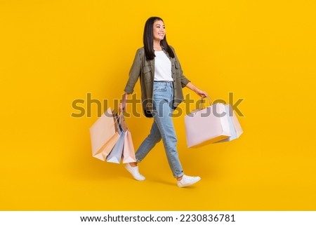 Full body photo of young positive good mood clothes designer korean girl hold packages from shopping walking boutique isolated on yellow color background