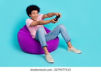Full body photo of young professional console player funny chevelure sit beanbag gaming zone advert hold joystick isolated on blue color background