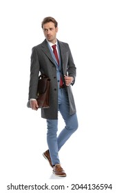 Full Body Picture Of Cool Elegant Fashion Man With Suitcase Fixing Coat And Looking To Side While Walking Isolated On White Background In Studio