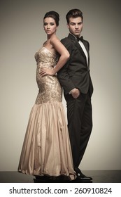 Full Body Picture Of A Elegant Couple Posing On Studio Background. He Is Holding Both Hands In His Pocket While She Is Looking At The Camera.