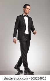 Full Body Picture Of An Elegant Man In Tuxedo Walking In Studio, Side View Picture On Grey Background