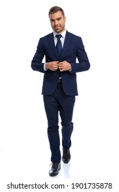 Full Body Picture Of Unshaved Young Man Smiling And Adjusting Navy Blue Suit, Walking Isolated On White Background In Studio